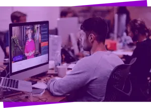 Imagem com filtro roxo de um homem sentado assistindo um curso em vídeo Descola no computador